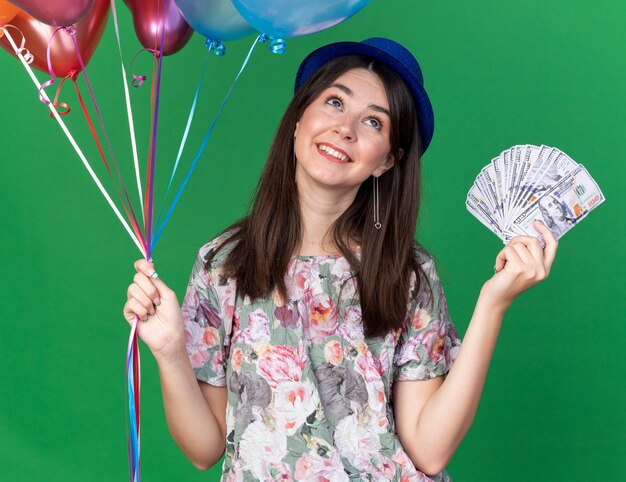 Souriant en levant la belle jeune fille portant un chapeau de fête tenant des ballons avec de l'argent