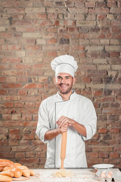 Souriant mâle boulanger debout derrière la table avec de la pâte et du pain