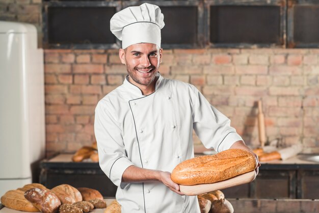 Souriant mâle boulanger tenant du pain cuit sur la planche à découper