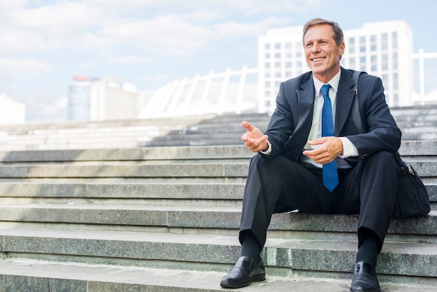 Souriant mature homme d&#39;affaires faisant le geste de la main assis sur l&#39;escalier