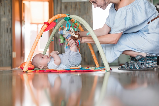 Souriant mère jouant avec son bébé allongé sur un tapis en développement sur le sol réfléchissant