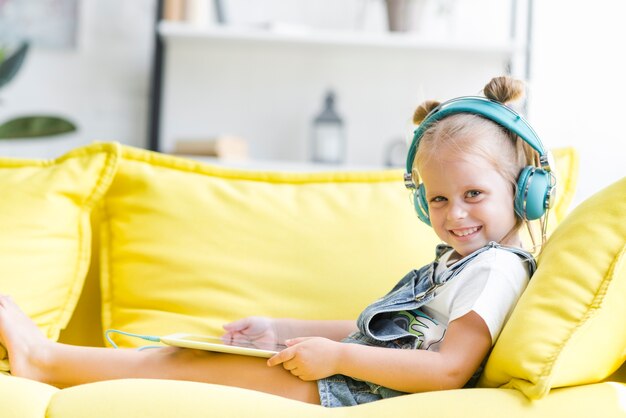 Souriant mignonne petite fille dans les écouteurs en écoutant de la musique en utilisant une tablette