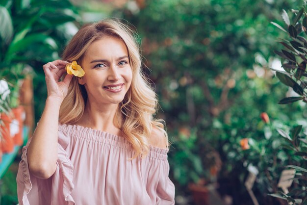 Souriant portrait de jeune femme blonde tenant une fleur jaune dans son oreille