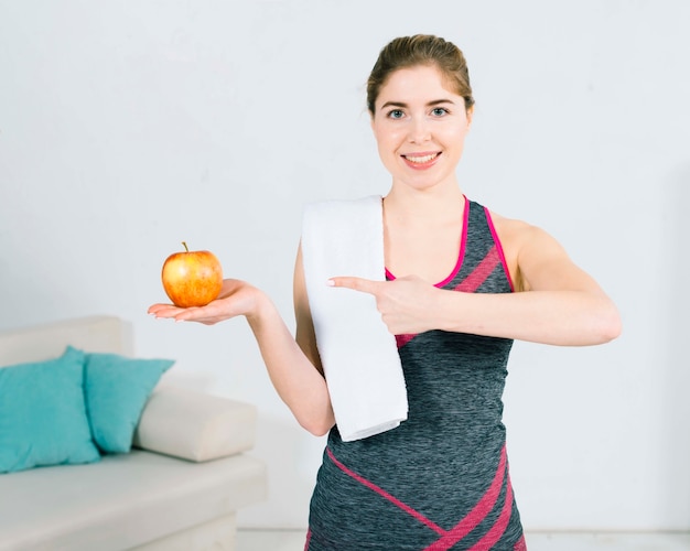 Souriant portrait de jeune femme fitness, pointant son doigt vers la pomme fraîche entière