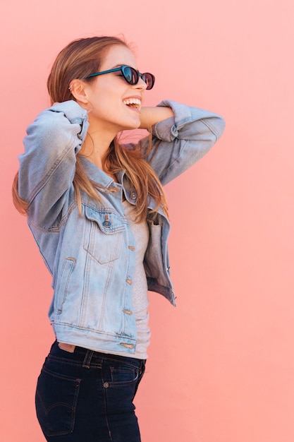 Souriant portrait d&#39;une jeune femme portant des lunettes de soleil sur fond rose