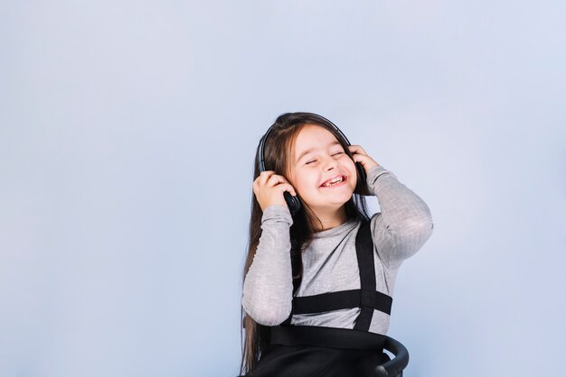 Souriant portrait d&#39;une jeune fille profitant de la musique au casque sur fond bleu