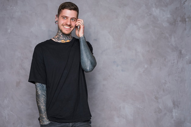 Photo gratuite souriant portrait d'un jeune homme tatoué aux oreilles percées, parlant au téléphone mobile