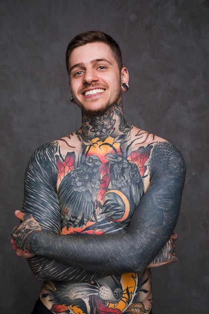 Photo gratuite souriant portrait d'un jeune tatouage avec nez percé et oreilles debout sur fond gris