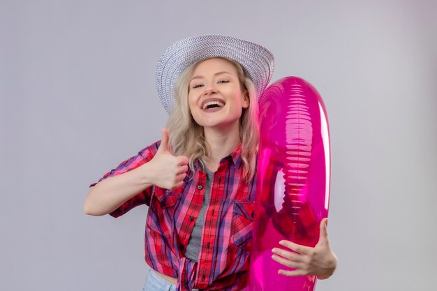 Souriant voyageur jeune fille portant une chemise rouge au chapeau tenant une bague gonflable sur fond blanc isolé