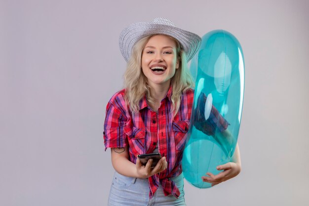 Souriant voyageur jeune fille portant une chemise rouge tenant une bague gonflable et un téléphone sur fond blanc isolé