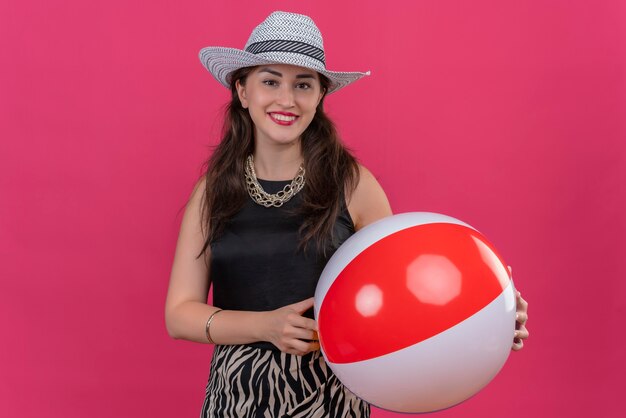 Souriant Voyageur Jeune Fille Portant Un Maillot De Corps Noir En Chapeau Tenant Ballon Gonflable Sur Fond Rouge