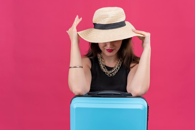 Souriant voyageur jeune fille portant un maillot de corps noir a mis les mains sur un chapeau sur fond rouge