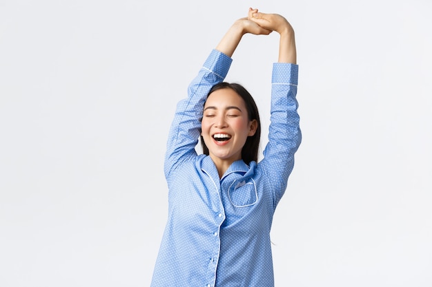 Souriante Belle Fille Asiatique En Pyjama S'étirant Avec Un Visage Satisfait, Bâillant Les Yeux Fermés, Bien Dormi Ou Sieste, Se Réveillant Le Matin. Femme En Pyjama Profitant De La Routine Matinale