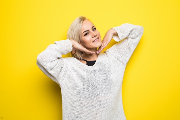 Souriante belle jeune femme blonde en pull blanc posant sur jaune