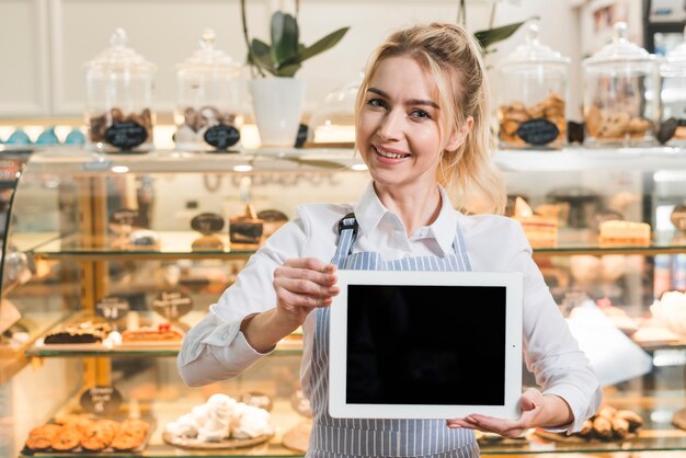 Souriante belle jeune femme debout devant une vitrine montrant une ardoise vierge