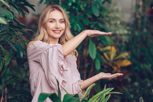 Souriante belle jeune femme montrant quelque chose sur les paumes de ses mains dans le jardin