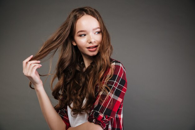 Souriante belle jeune femme toucher ses cheveux et regarder ailleurs