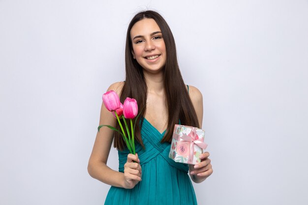 Souriante belle jeune fille tenant un cadeau avec des fleurs