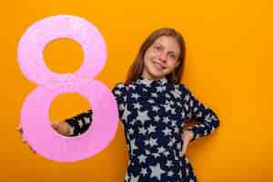 Photo gratuite souriante belle petite fille le jour de la femme heureuse tenant le numéro huit à la caméra isolée sur le mur orange