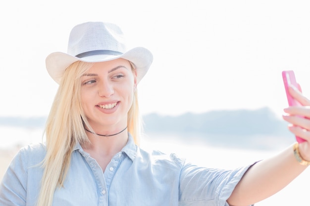 Souriante blonde jeune femme prenant selfie de téléphone portable
