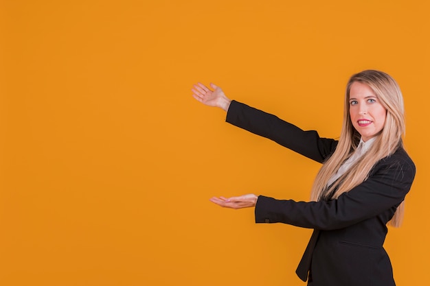 Souriante blonde jeune femme présentant un fond orange