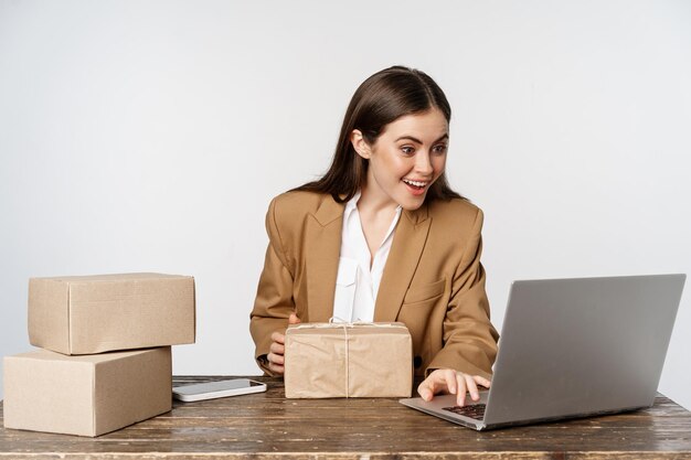 Souriante femme d'affaires heureuse travaillant dans son bureau avec des commandes de processus de livraison de colis sur son ordinateur portable...