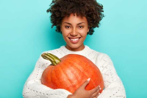 Photo gratuite souriante fille aux cheveux bouclés positive en pull blanc, tient la citrouille d'automne, étant en pleine forme