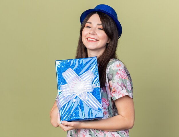 Souriante jeune belle fille portant un chapeau de fête tenant une boîte-cadeau