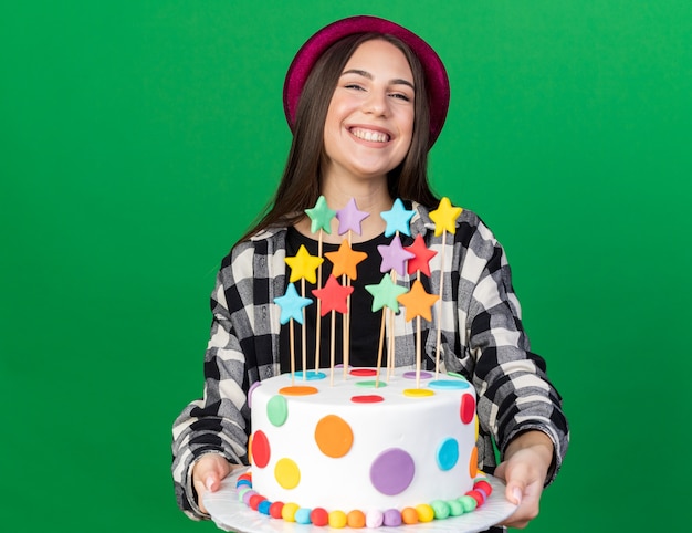 Souriante jeune belle fille portant un chapeau de fête tenant un gâteau