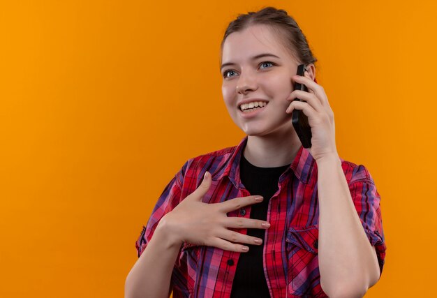 Souriante jeune belle fille portant une chemise rouge parle au téléphone sur fond jaune isolé avec espace de copie