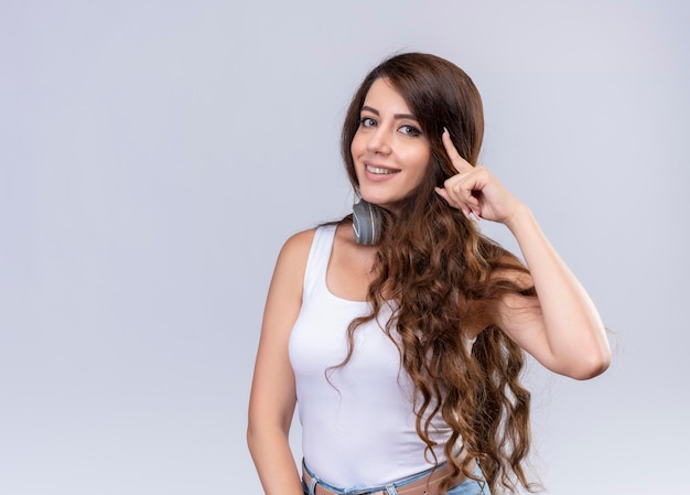 Souriante jeune belle fille portant des écouteurs sur le cou mettant le doigt sur le temple avec espace copie