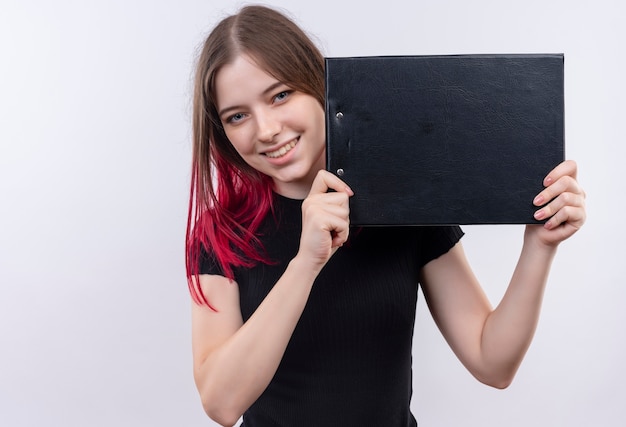 Souriante jeune belle fille portant un t-shirt noir tenant le presse-papiers sur fond blanc isolé avec espace copie