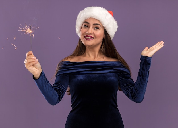 Souriante Jeune Belle Fille Vêtue D'une Robe Bleue Et Chapeau De Noël Tenant Des Cierges étalant La Main Isolé Sur Fond Violet