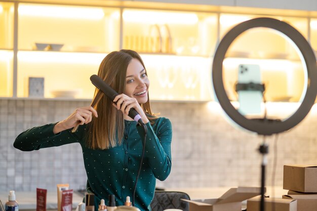 Souriante jeune coiffeuse montrant comment utiliser le fer à lisser