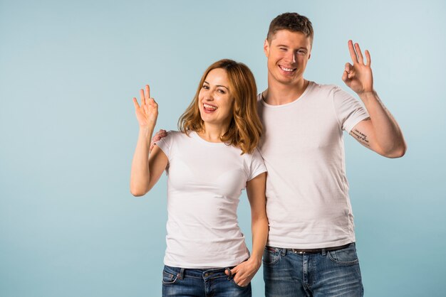 Souriante jeune couple montrant le geste de signe ok sur fond bleu