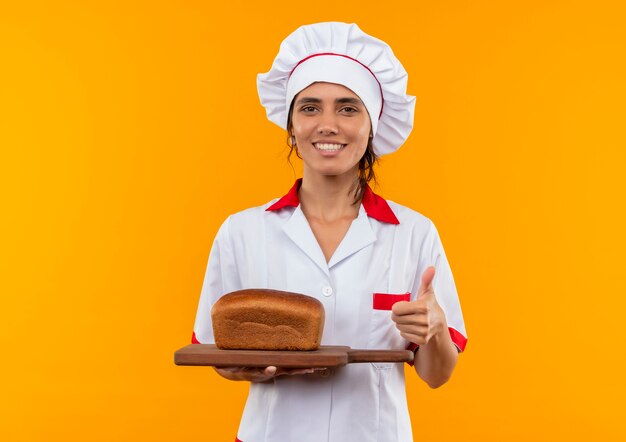 Souriante jeune cuisinière portant l'uniforme de chef tenant du pain sur la coupe de son pouce vers le haut avec copie espace