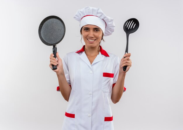 Souriante jeune cuisinière portant l'uniforme de chef tenant une poêle et une spatule avec espace de copie