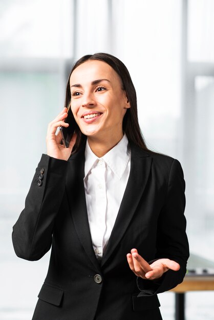 Souriante jeune femme d&#39;affaires prenant sur téléphone portable haussant les épaules