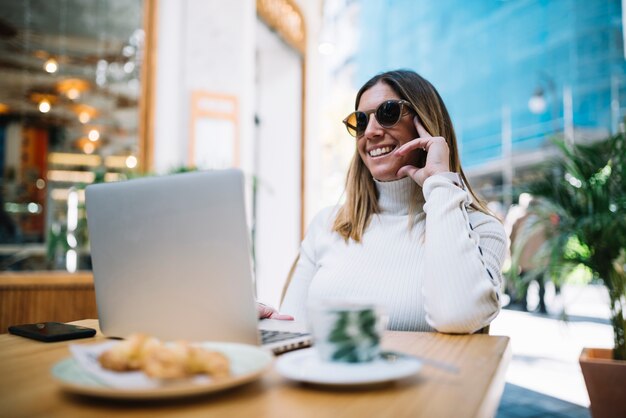 Souriante jeune femme à l&#39;aide d&#39;un ordinateur portable à table avec boisson et croissants au café de rue