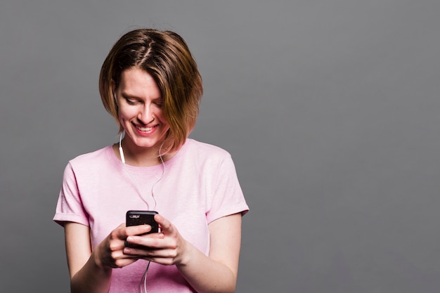 Souriante jeune femme à l&#39;aide de téléphone portable contre le mur gris