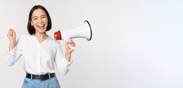 Souriante Jeune Femme Asiatique Posant Avec Le Concept De Mégaphone D'annonce De Nouvelles Et D'informations Debout Sur Fond Blanc