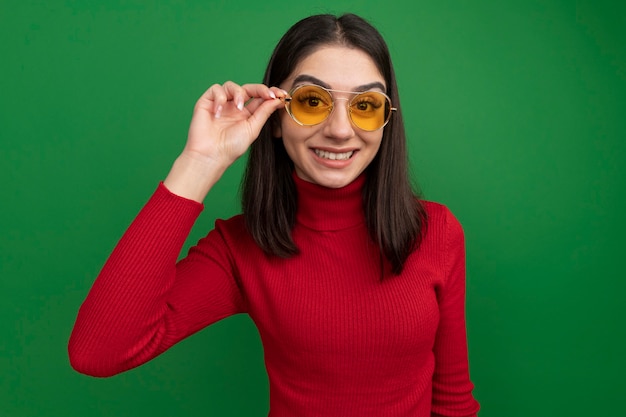 Souriante jeune femme assez caucasienne portant et attrapant des lunettes de soleil