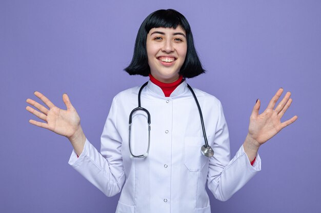 Souriante jeune femme assez caucasienne en uniforme de médecin avec stéthoscope gardant les mains ouvertes