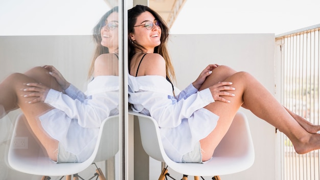 Souriante jeune femme assise sur une chaise blanche sur le balcon