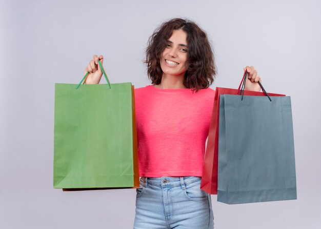 Souriante jeune femme belle tenant des sacs en carton sur un mur blanc isolé