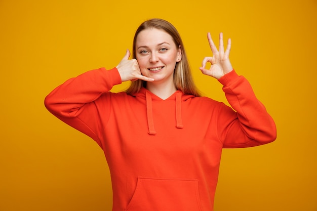 Souriante jeune femme blonde faisant le geste d'appel et signe ok