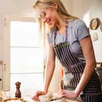 Photo gratuite souriante jeune femme blonde, pétrir la pâte sur une planche à découper à la maison