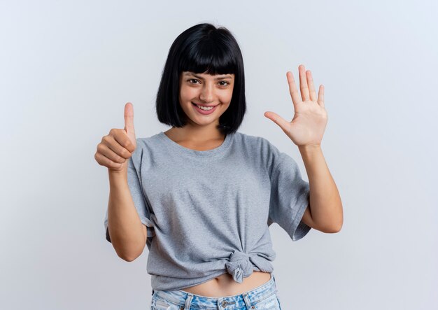 Souriante jeune femme brune caucasienne fait six gestes avec les doigts