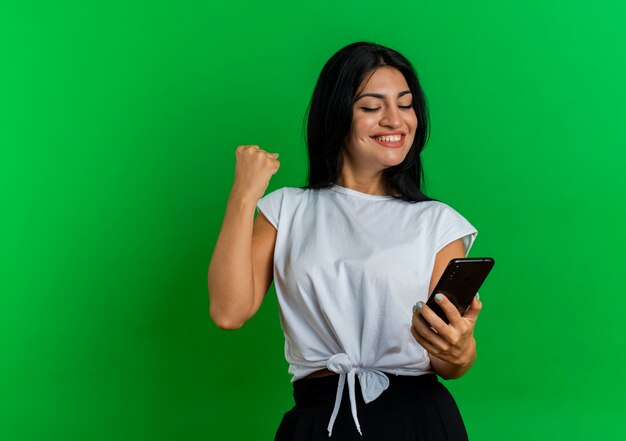 Souriante jeune femme caucasienne garde le poing en regardant le téléphone