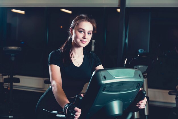 Souriante jeune femme à cheval sur un vélo d&#39;exercice dans la salle de gym